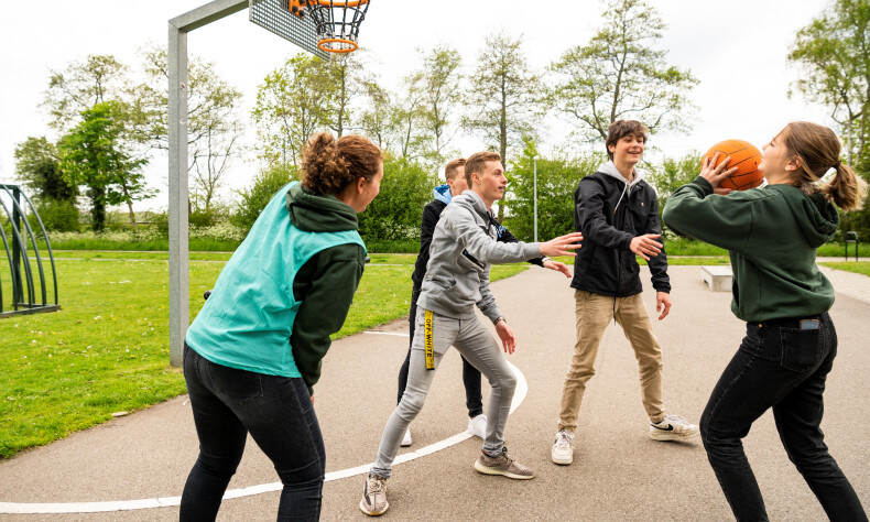 Een paar jongeren spelen basketbal op een asfalten basketbalveldje