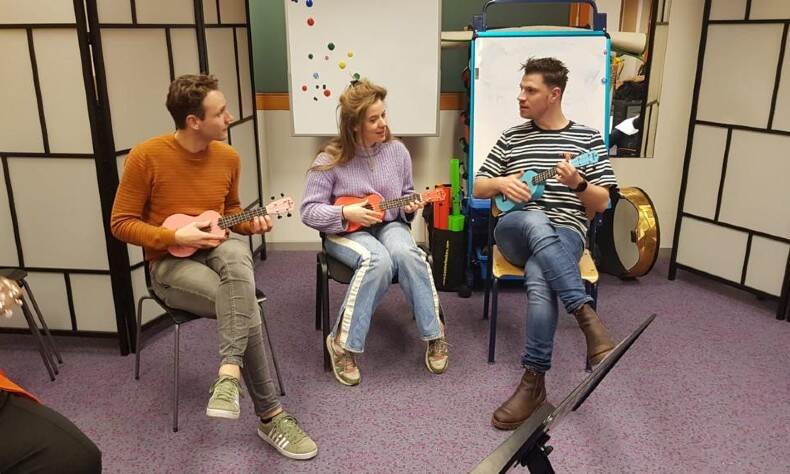 Drie mensen zitten in een klaslokaal en leren ukelele